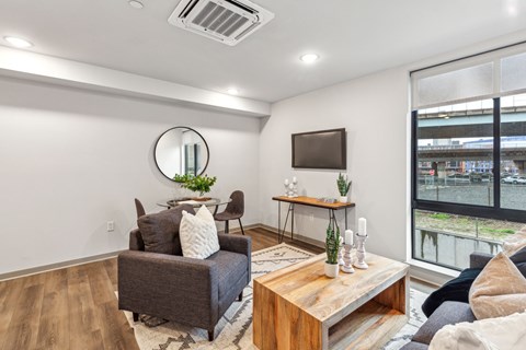 A living room with a grey couch, a wooden coffee table, and a round mirror on the wall.