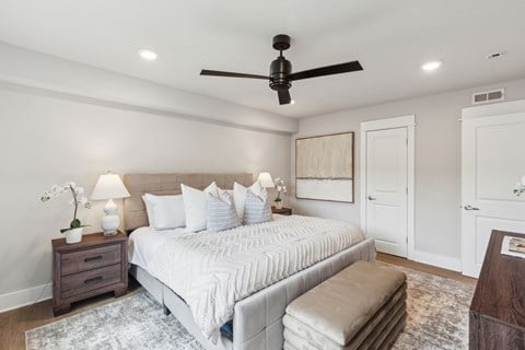 A bedroom with a large bed, a ceiling fan, and a rug on the floor.