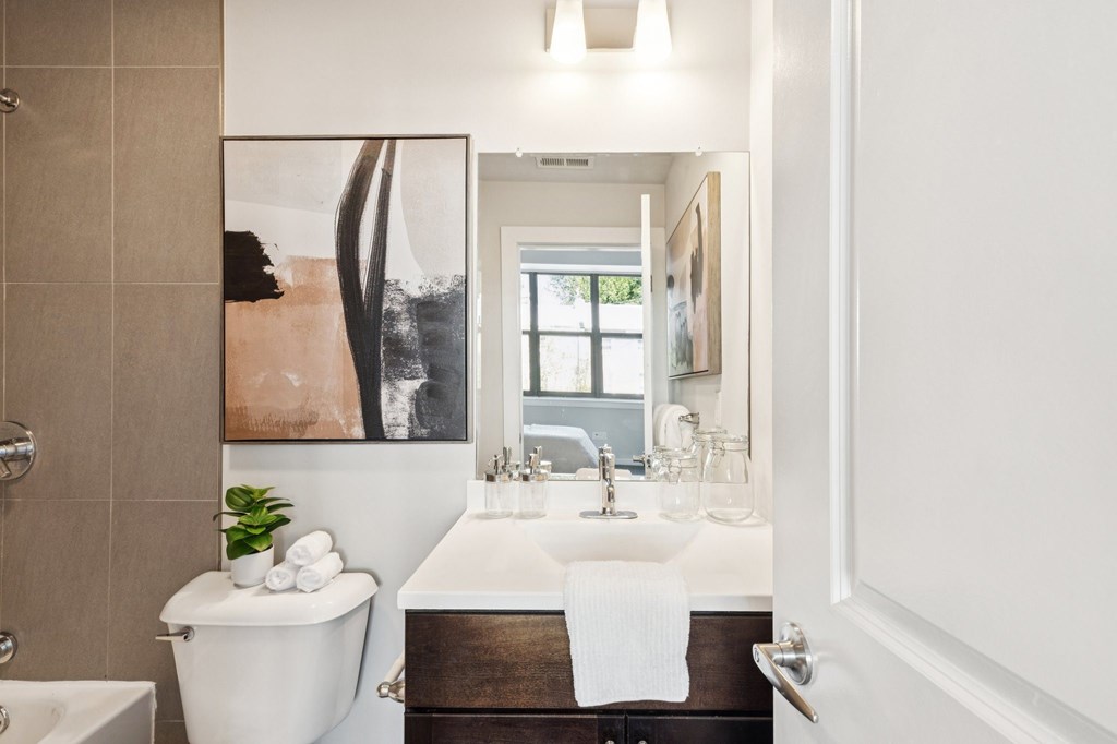 A bathroom with a white toilet, a white sink, and a large painting on the wall.