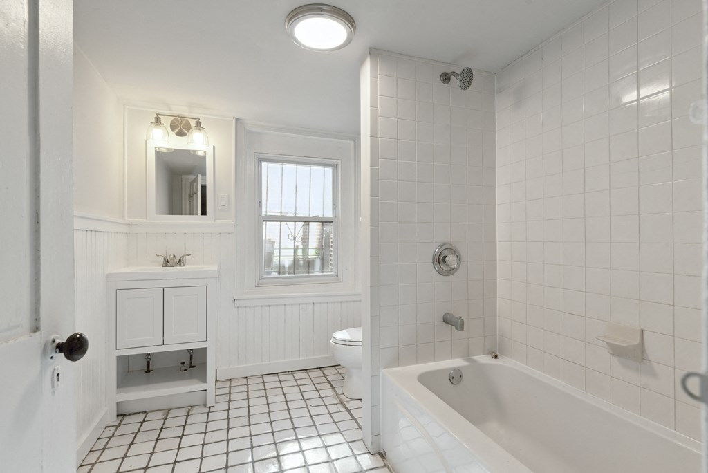 a bathroom with white tiles and a white bathtub