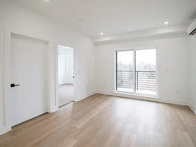 A room with a white door, a window with blinds, and a wooden floor.