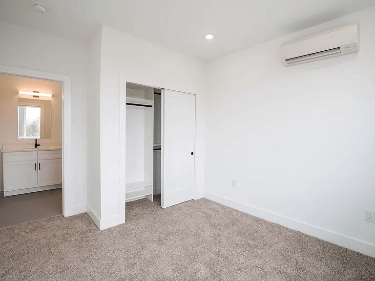 A room with a carpeted floor and a white wall with a door and a window.