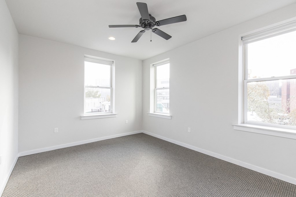 an empty room with three windows and a ceiling fan