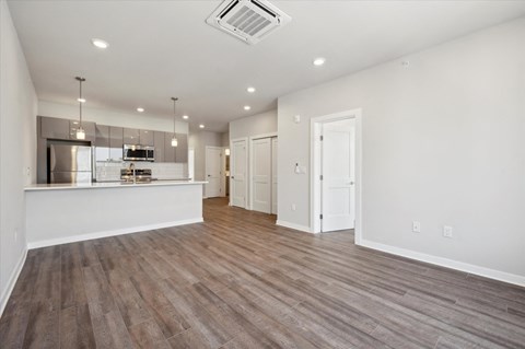 an empty living room with a kitchen in the background