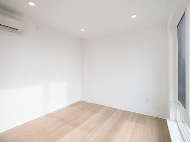 A room with wooden flooring and a window on the right side.