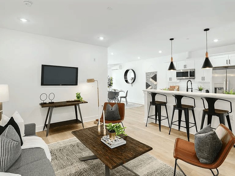 A modern living room with a grey couch, a wooden coffee table, and a bar area in the background.