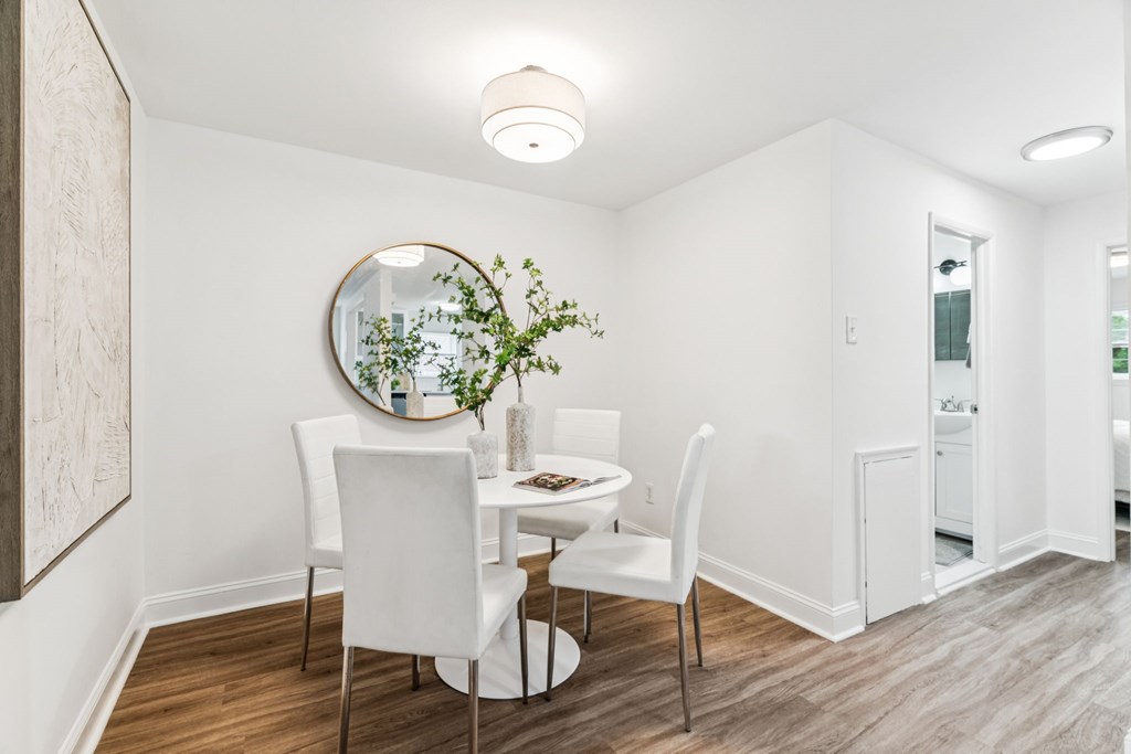 A white dining room with a round mirror and a potted plant on the table.