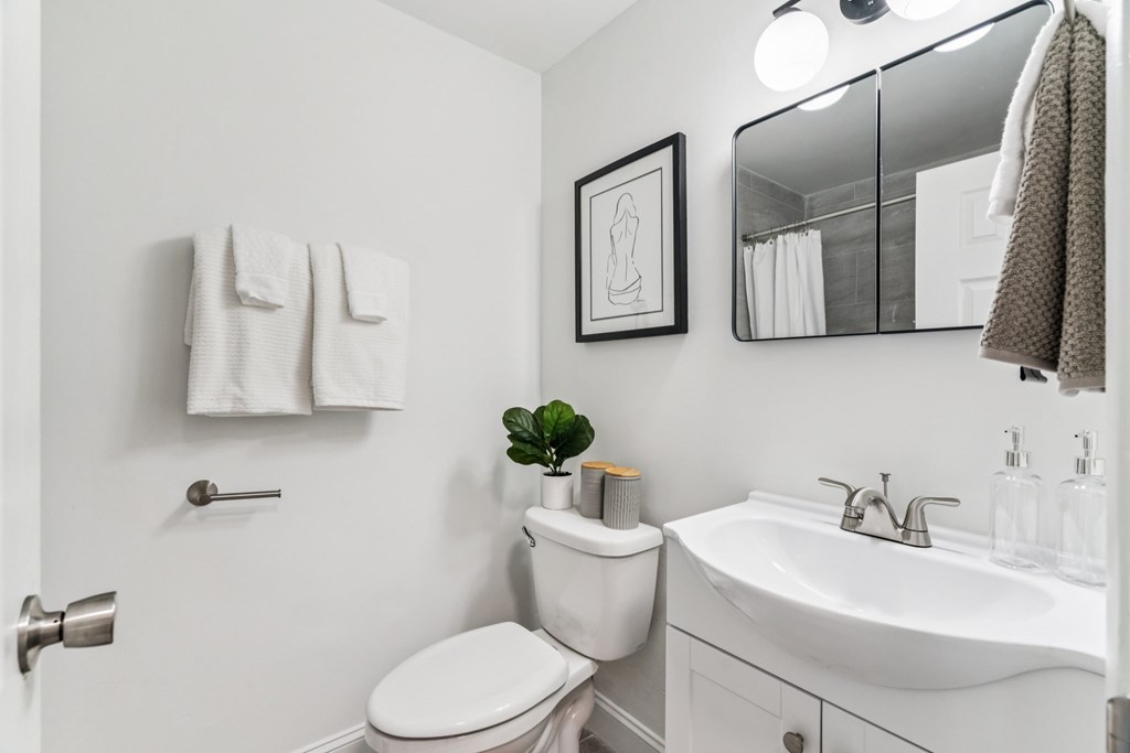 A white bathroom with a toilet, sink, mirror, and towel rack.