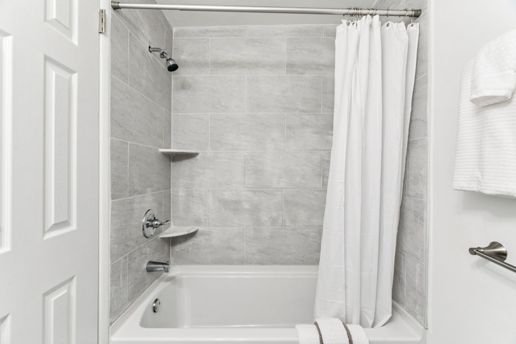A white bathroom with a tub, shower, and towel rack.