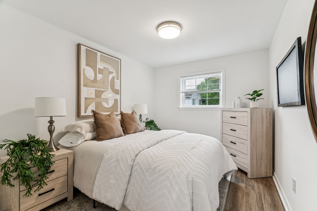 A bedroom with a large bed, a lamp, and a plant.