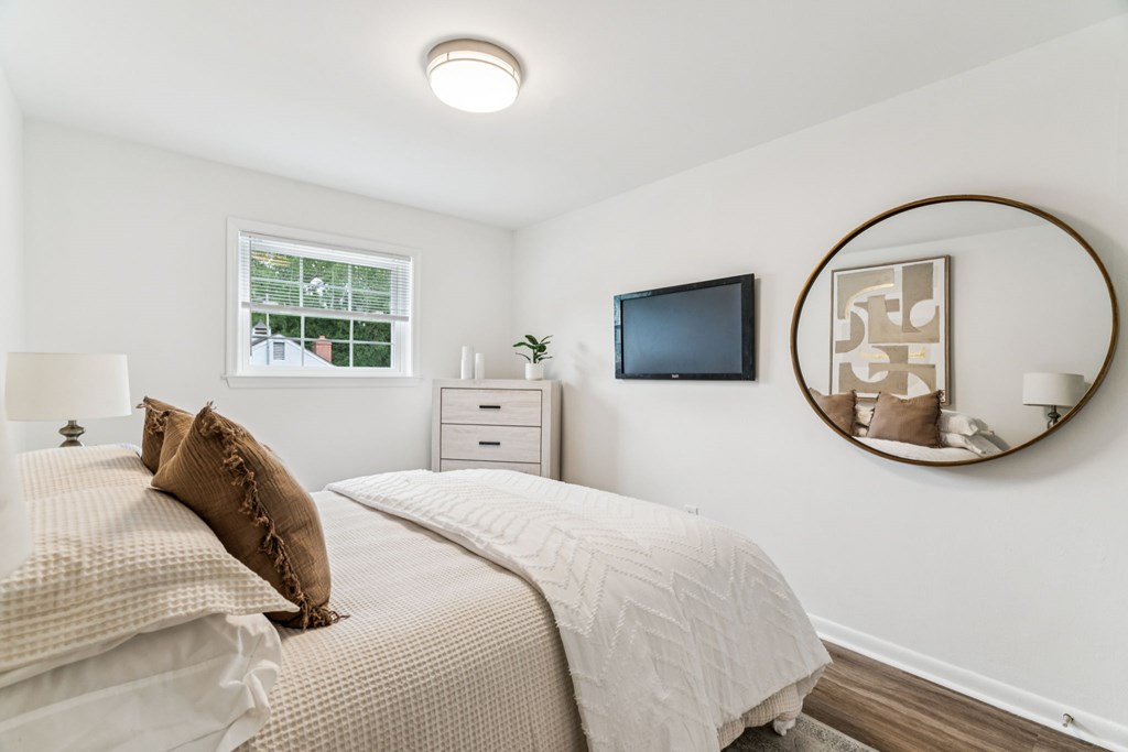 A bedroom with a bed, nightstand, and a mirror with a plant on it.