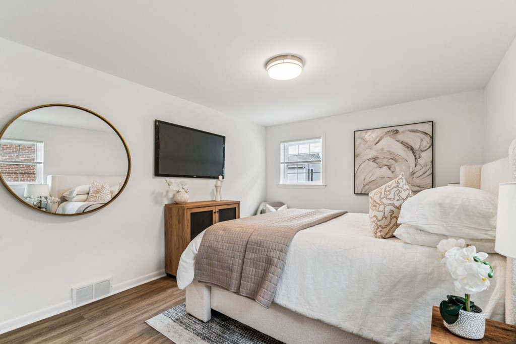 A bedroom with a bed, a round mirror, a TV, and a vase of flowers.