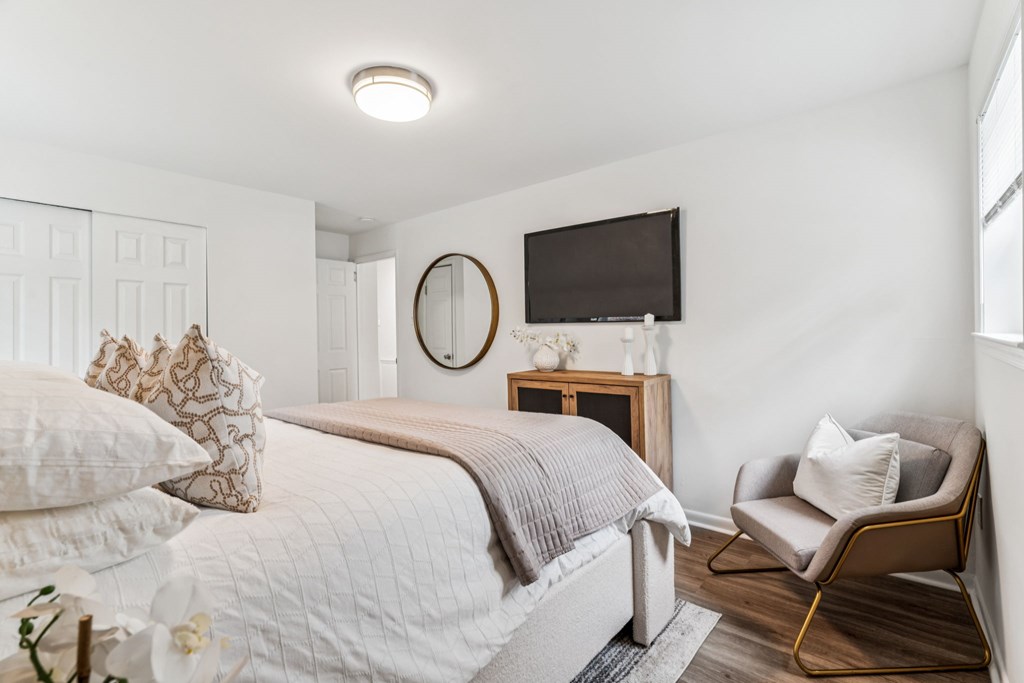 A bedroom with a bed, chair, and a mirror.