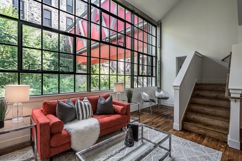 A red couch with pillows and a white fur throw sits in a living room with a glass table in front of it.