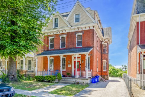 a red brick house with a porch and a tree