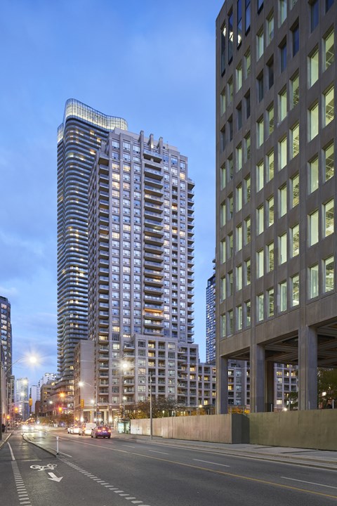 A tall building with a curved top stands next to a shorter building with a grid-like facade.