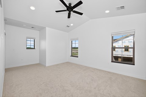 A spacious room with a ceiling fan and two windows.
