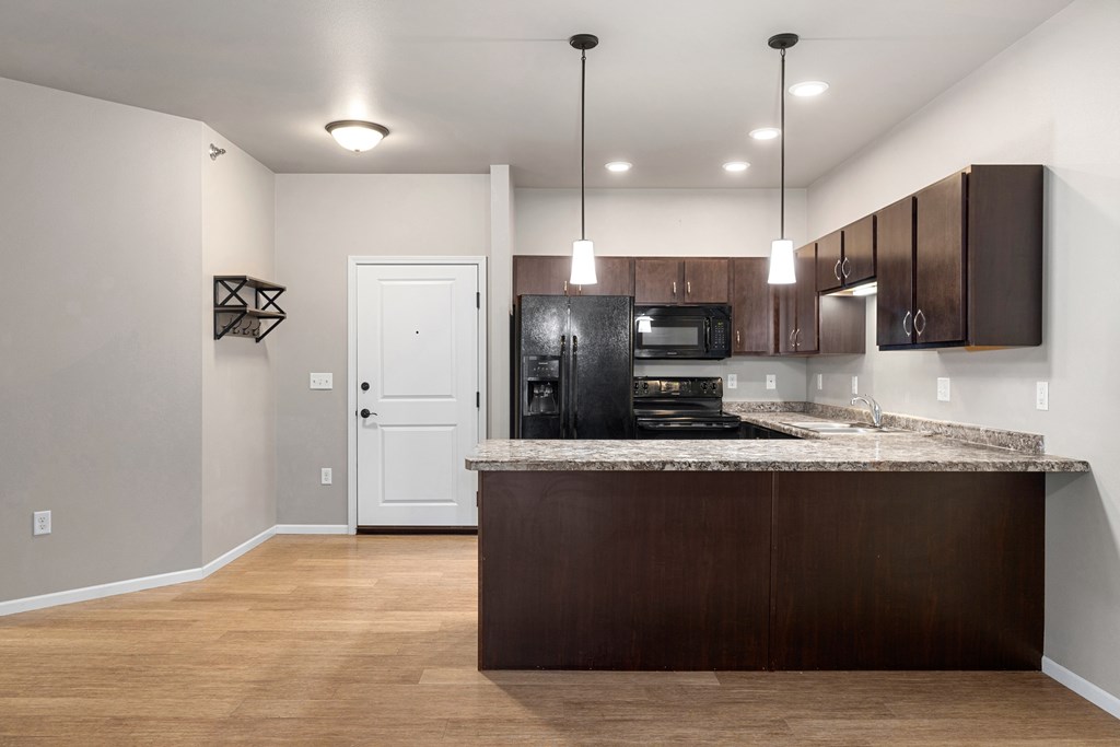 A kitchen with a black refrigerator and brown cabinets.