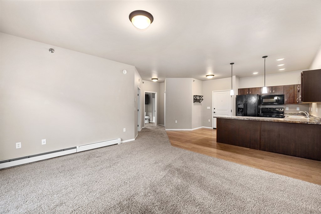 A spacious living room with a grey carpet and a wooden cabinet.