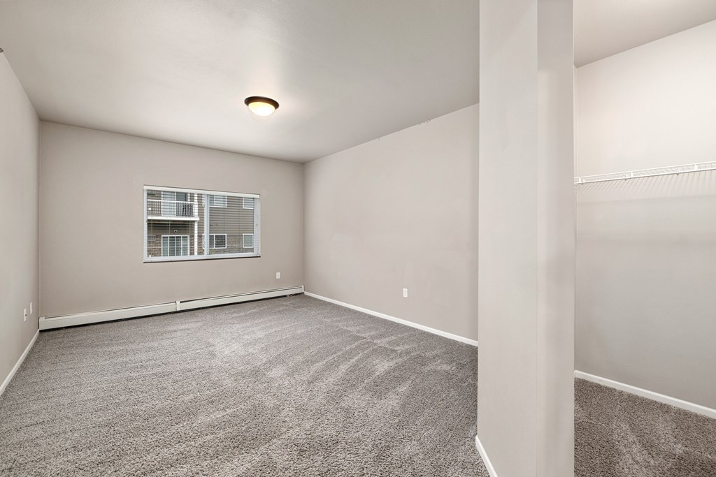 A sparsely furnished room with a window and carpeted floor.