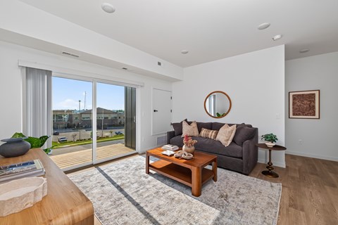 A living room with a grey couch, a wooden coffee table, and a round mirror on the wall.
