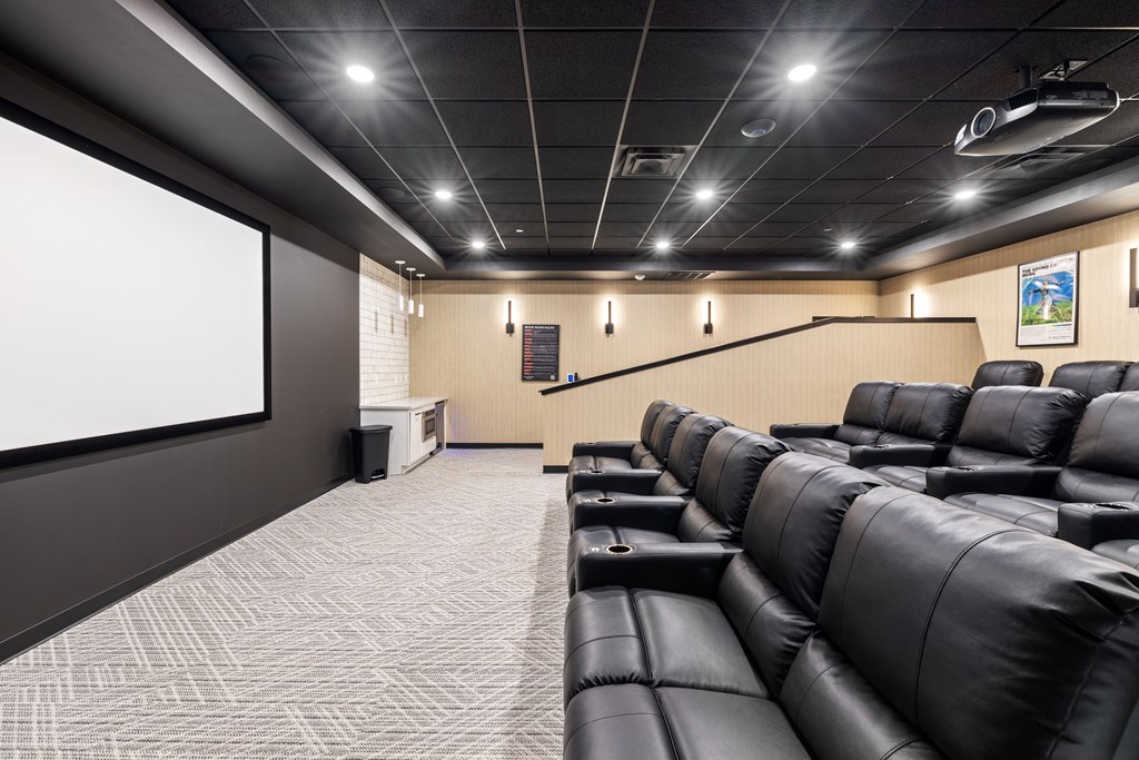 A modern home theater with black leather seats and a large screen.