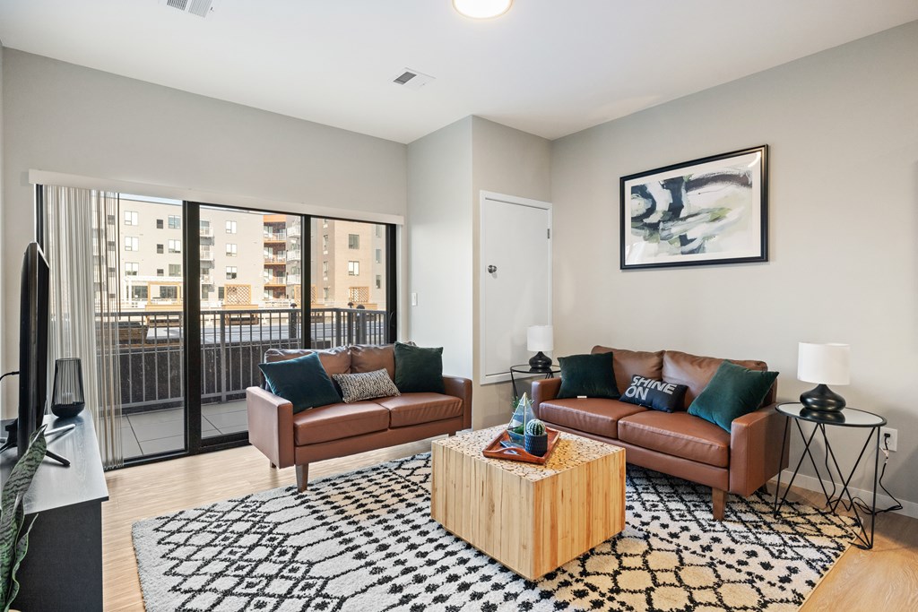 A living room with a brown couch, a black and white rug, and a painting on the wall.