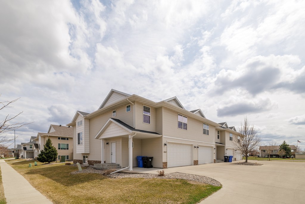 A large, modern house with a driveway and a small tree in front.