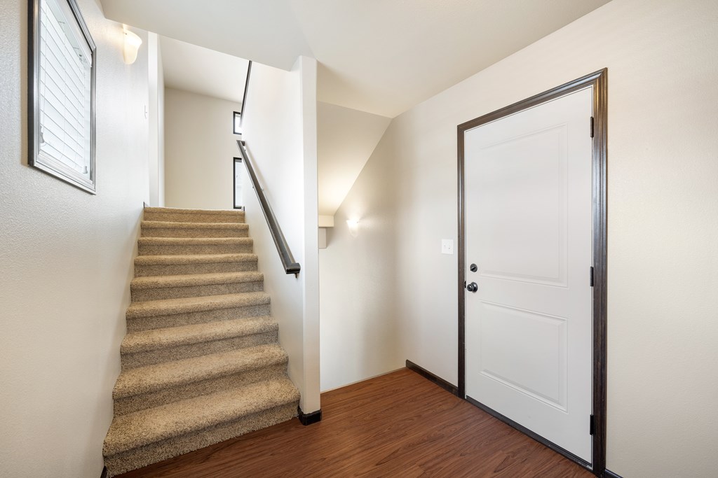 A staircase with a carpeted runner leads up to a white door.