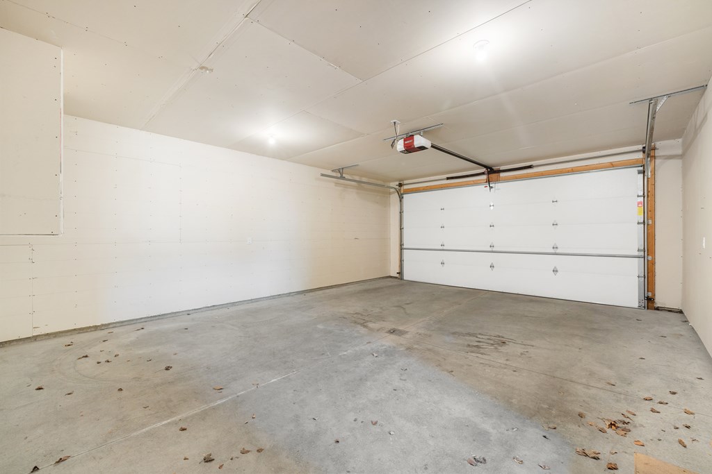 A large empty garage with a white door and a red light on the ceiling.