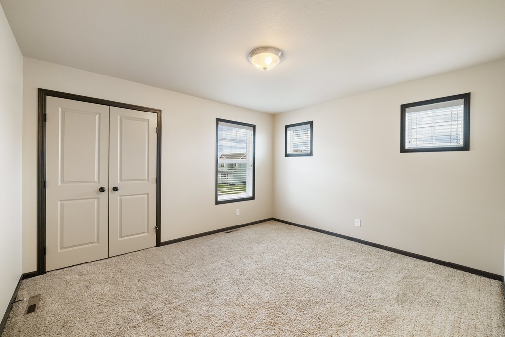 A room with a carpeted floor, a door, a window with blinds, and a picture on the wall.