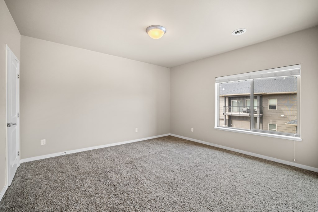 A room with a carpeted floor and a window showing a view of a building.