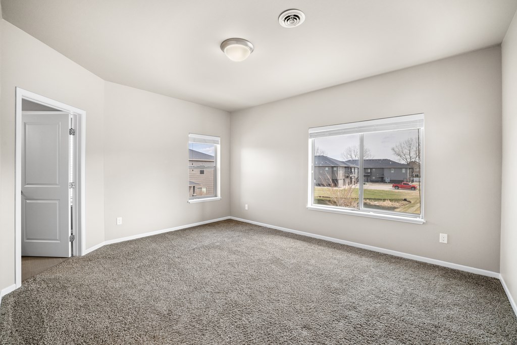 A room with a grey carpet and a window showing a residential area outside.
