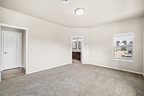 A spacious room with a door, a window, and a carpeted floor.