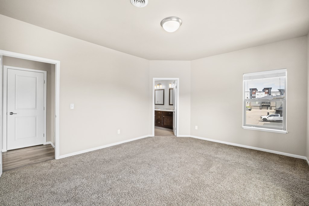 A spacious room with a door, a window, and a carpeted floor.