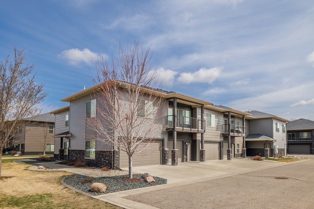 A modern two-story apartment building with a grey and beige exterior and a small tree in front.