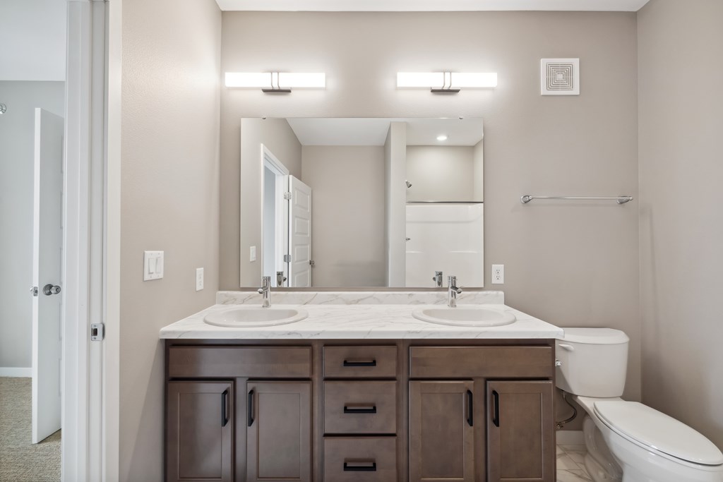 A bathroom with double vanity with wood-toned cabinets.