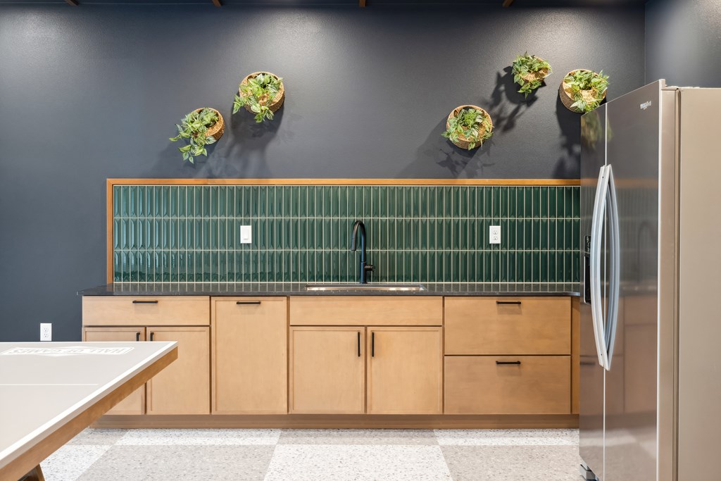 Kitchenette with green backsplash and light colored wood cabinets.