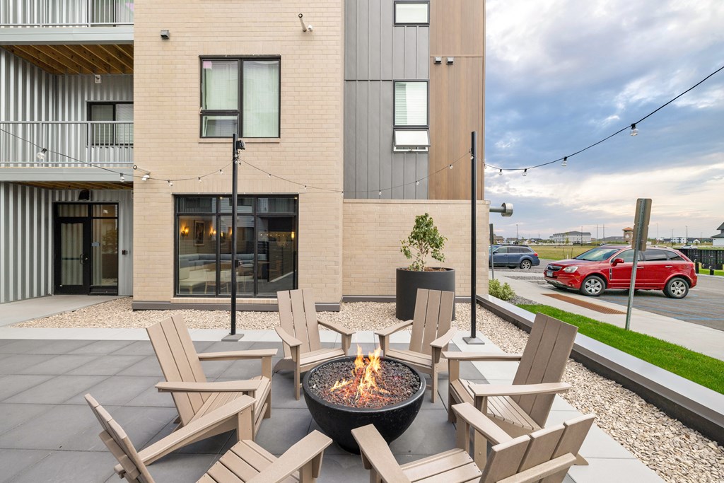 A patio with chairs and a fire pit in front of a modern building.