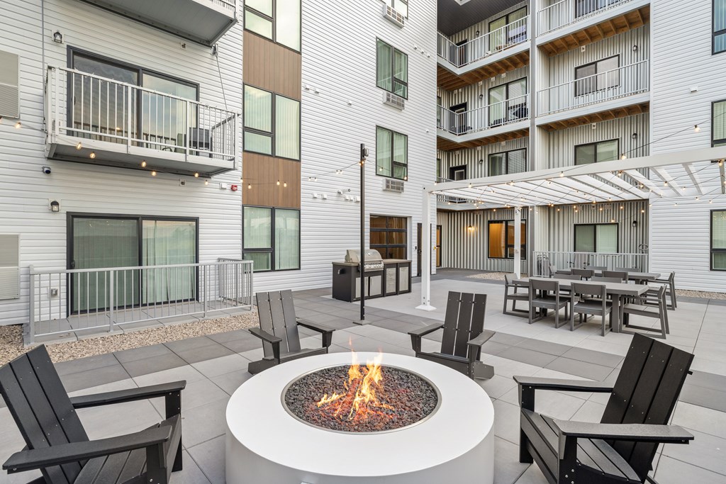 A fire pit sits in the middle of a patio surrounded by chairs.