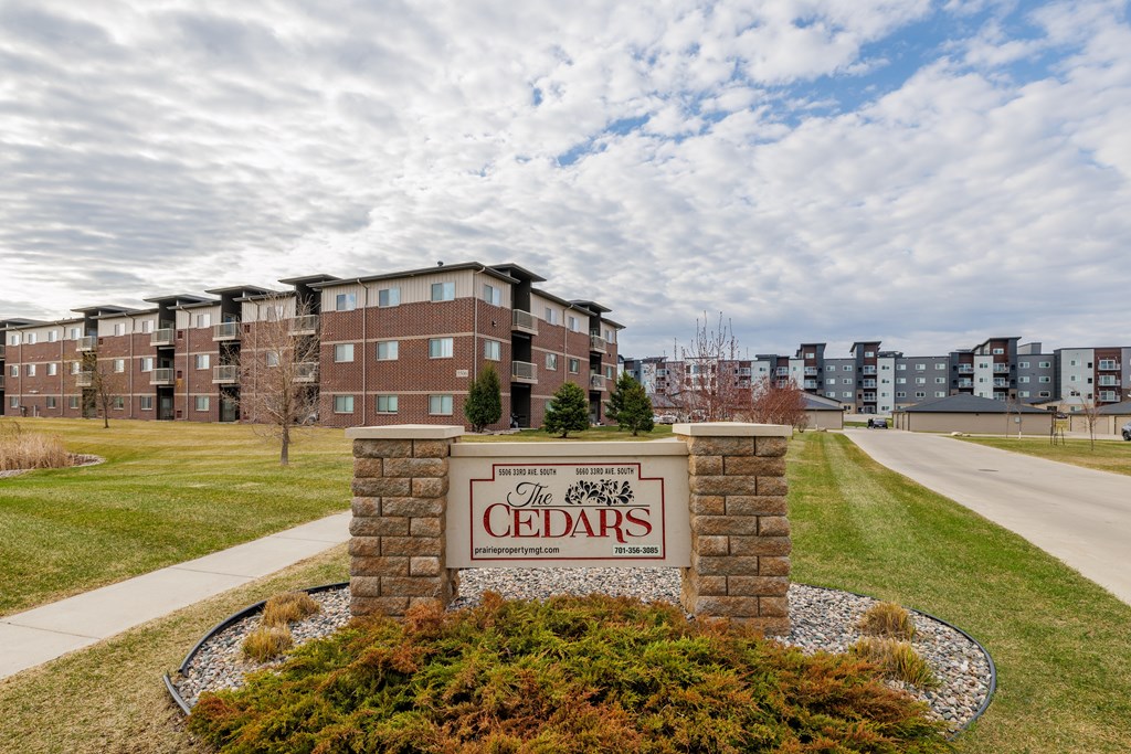 The Cedars apartment complex is surrounded by a well-maintained lawn and a clear sky.