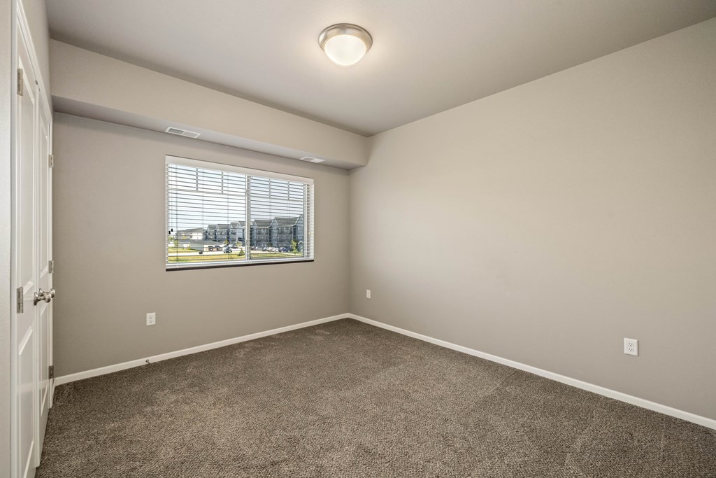 A room with a carpeted floor and a window with blinds.
