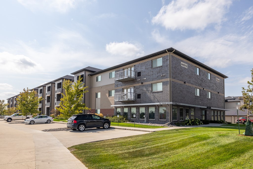 A grey apartment building with cars parked in front.