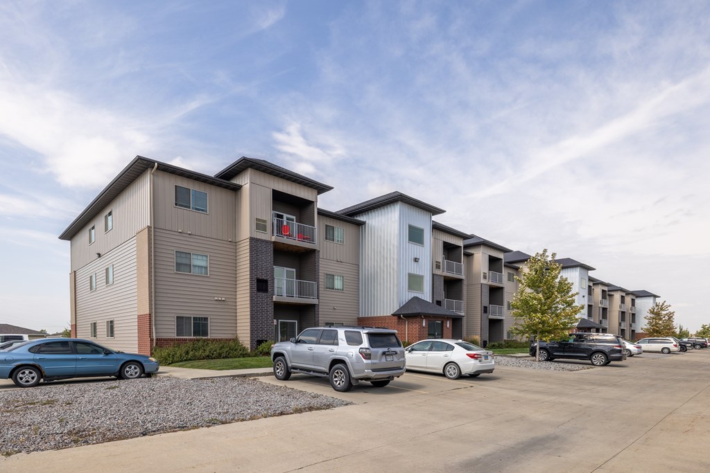 A row of apartment buildings with cars parked in front.