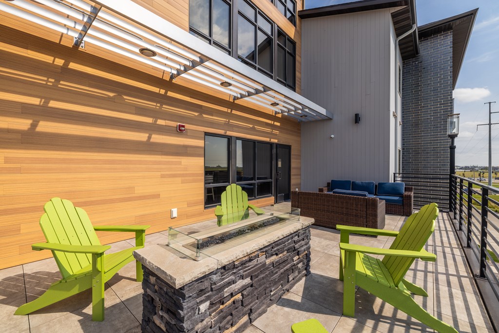 A patio with a stone fireplace and green chairs.