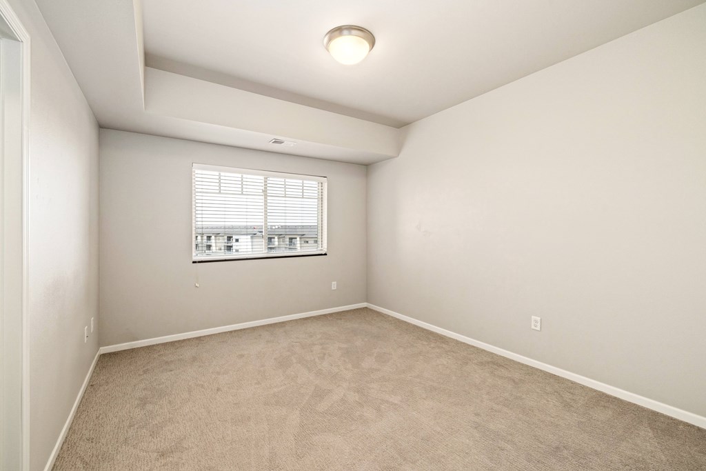 A room with a carpeted floor and a window with blinds.