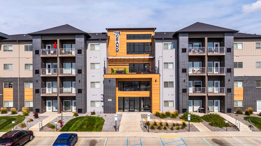 A large apartment complex with a central building entrance and cars parked in the driveway.