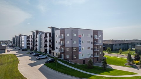 A row of apartment buildings with cars parked in front.