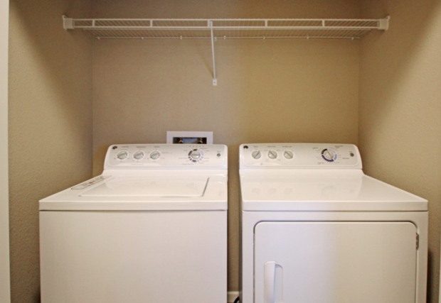 two washes and dryers in a room with a rack on the wall above