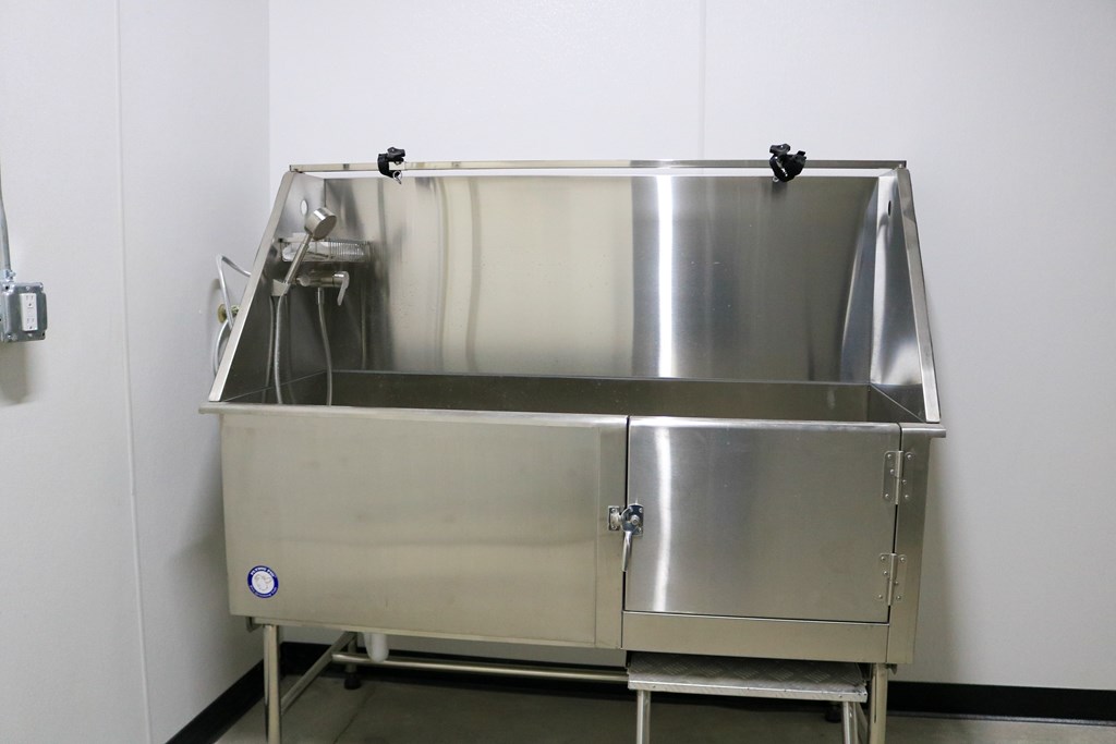 A large stainless steel sink with a faucet and a drain is installed in a white wall.